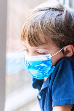 マスクを着用して悲しそうに窓の外を見つめる小さな男の子