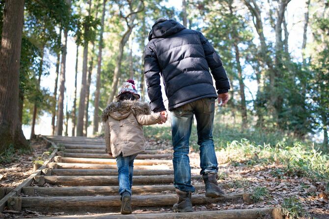 手をつないで森を歩く父と娘