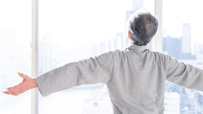 朝の窓際で体を伸ばす高齢男性