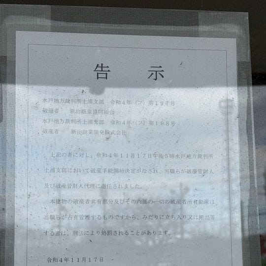 閉鎖された入口に掲示されている、新治商業協同組合と新治商業開発に関する破産告示書類。