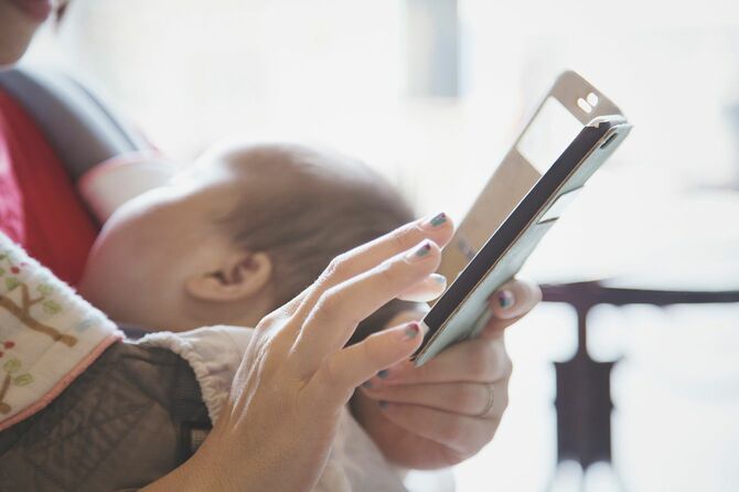 ベビーキャリアで彼女の赤ちゃんの女の子を運ぶスマートフォンを使用して母親の手