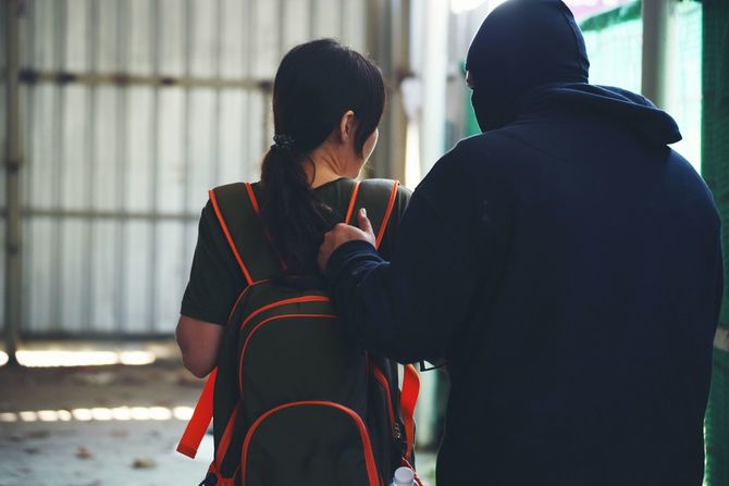 背後から女性のリュックサックに手をかける黒づくめの男性