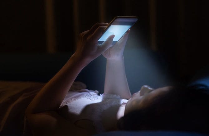 ベッドに仰向けになり、スマホを閲覧している女性