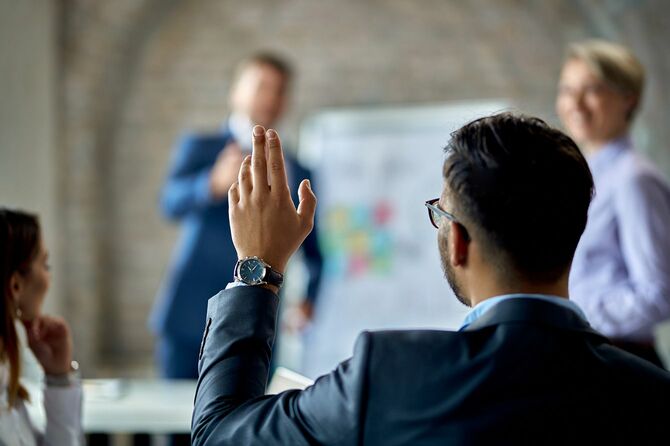 会議中に意見を述べるために手を挙げる人