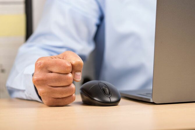 オフィスでパソコンの前で拳を握り怒っている男性