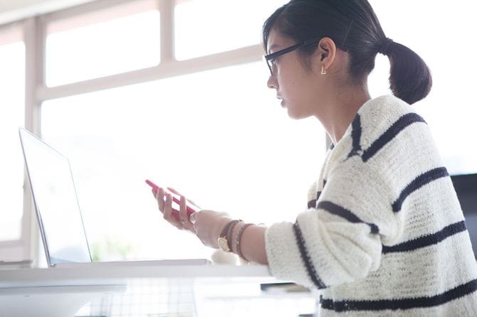 パソコンを前にスマホを持って座っている女性