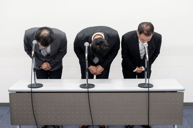 謝罪会見で頭を下げる3人の人物