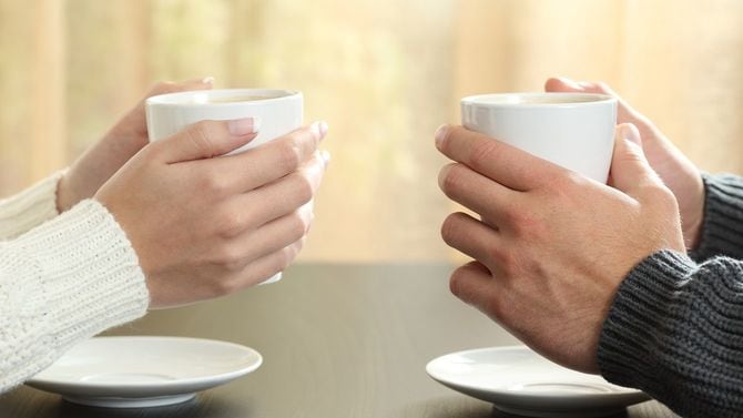 向かい合ってカップを手に持つカップルの手元