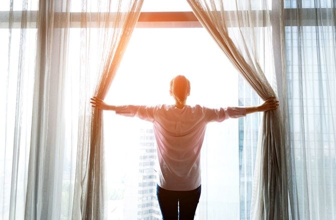 大きな窓のカーテンを開ける女性