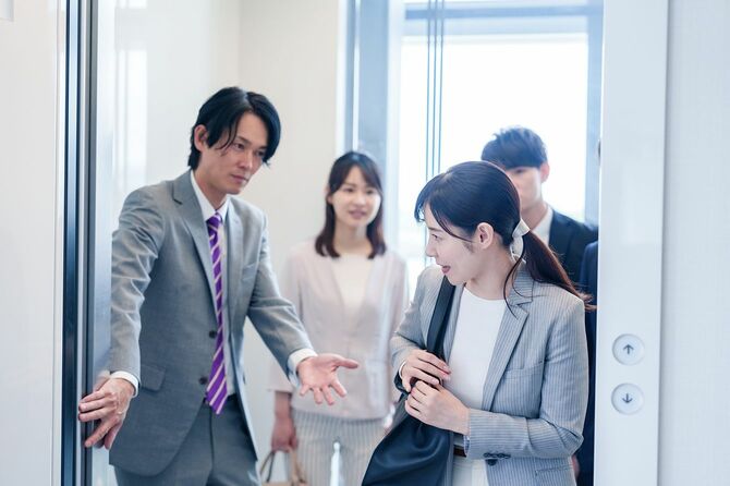 エレベーターの扉を抑えて誘導するビジネスパーソン