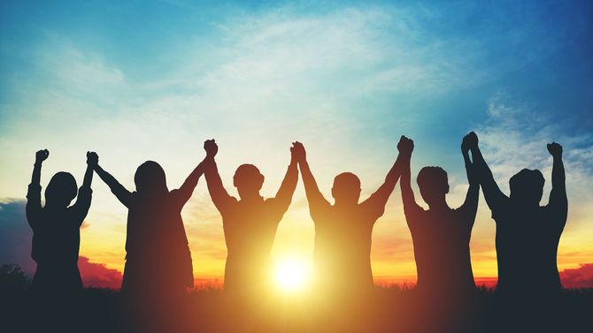 夕陽に向かって繋いだ手を挙げるビジネスチーム
