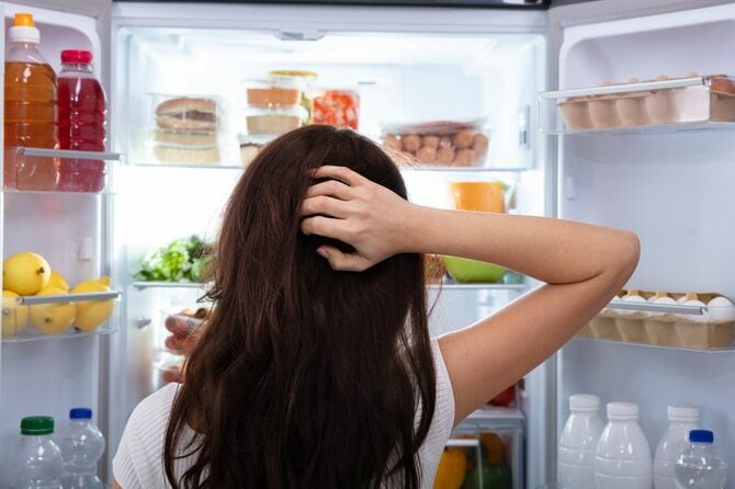 冷蔵庫の中の食品を見て頭を悩ませる女性