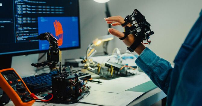 手につけたデバイスでロボットの手を遠隔操作する人