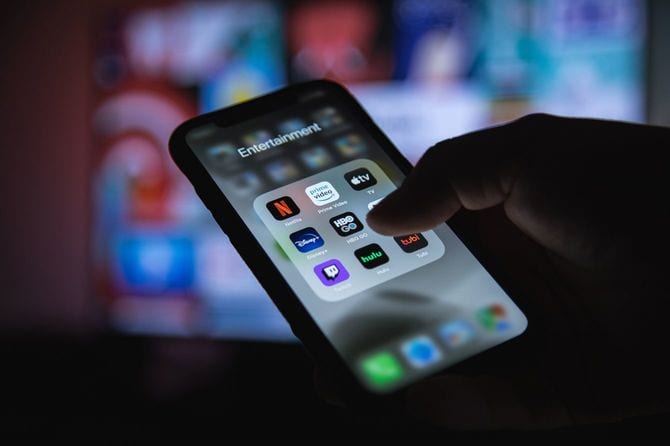 暗い部屋で、スマホの画面でストリーミングサービスを選択しようとしている手元