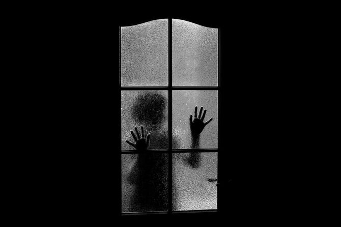 すりガラスの向こうから真っ暗なこちらの部屋をのぞいている子供のシルエット