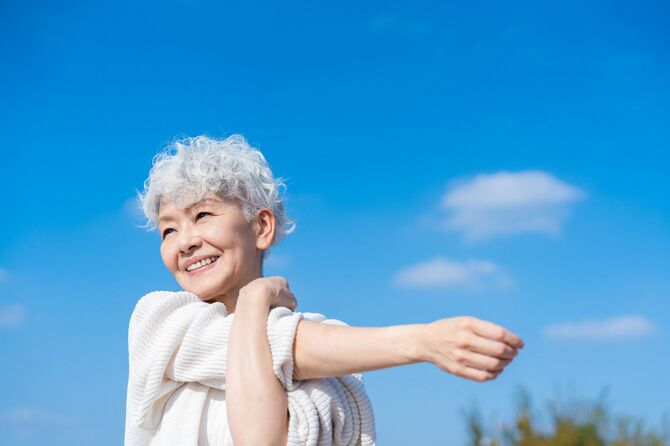 青空の下で伸びをする高齢女性