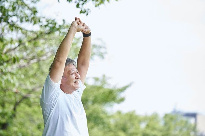 屋外で伸びをする高齢男性