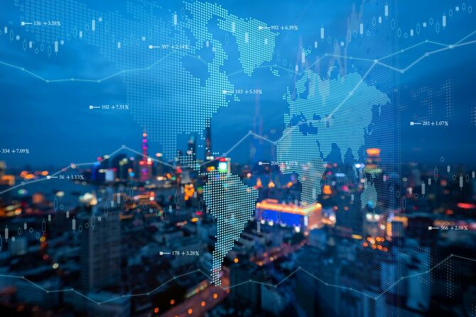 夕方を迎えた都市と、世界地図と動き続ける株式チャート