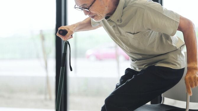 杖をついて立ち上がろうとする高齢男性