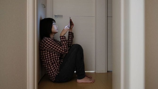暗い部屋で床に座り込んでスマホをみる女性