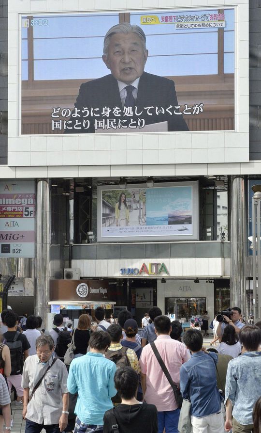 2016年8月、上皇さまのビデオメッセージを映す大型モニターを見る人たち＝東京・新宿