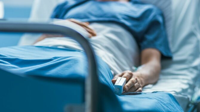 病院のベッドに横たわる男性、指にはパルスオキシメーター