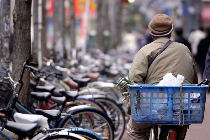 自転車にかごをくくりつけてゆっくりと街を行く、シニア男性