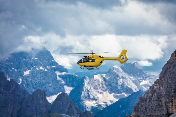 険しい山並みを飛んでいく山岳救助のヘリ