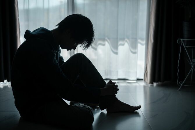 薄暗い部屋でうつむいて膝を抱える少年