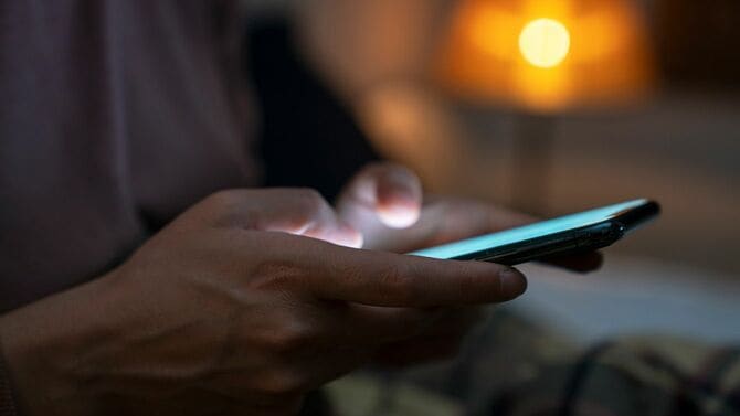 ベッドに座り、スマホをチェックしている女性の手元