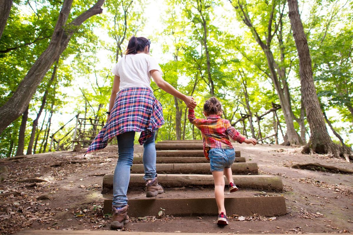手をつないで森の階段を上っている母と娘