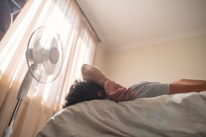 自宅で扇風機の近くで暑さに苦しむ男性
