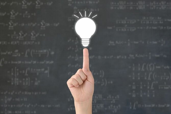 黒板を背景に指先に電球が光る手