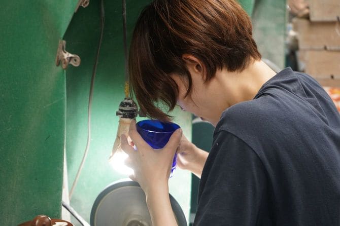 女性の職人が研磨機を使って江戸切子のカット加工をすすめる。