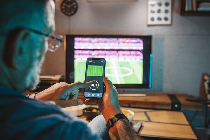 テレビでスポーツ観戦をしながらスマホを操る男性