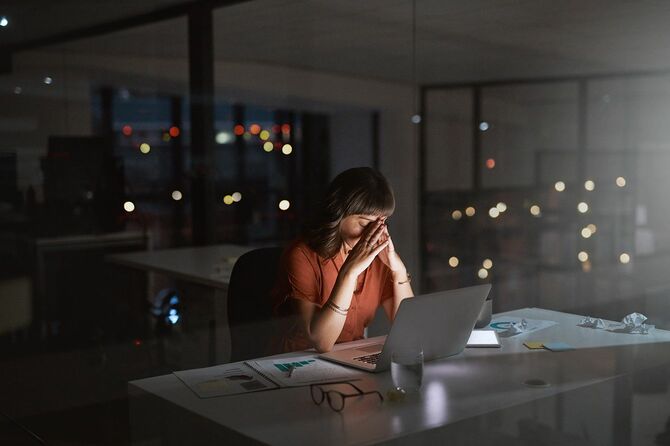 夜にオフィスでラップトップで作業している間にストレスを感じている若いビジネスウーマンのショット