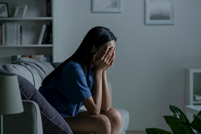 自宅のソファに座って、悲しみを感じ、メンタルヘルスのうつ病に苦しんでいることを心配しているアジアの若い女性。