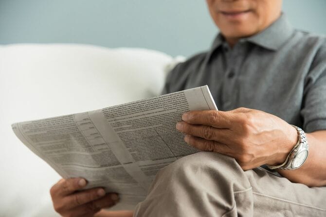 新聞を読みながら笑顔になる高齢男性