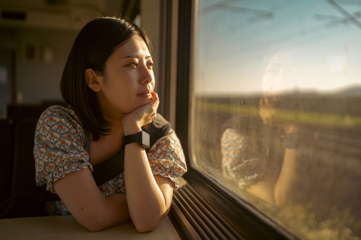 電車の車窓から外を眺める旅する若い女性観光客
