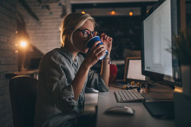 彼女のデスクトップコンピュータに座っている若い女性の写真, 彼女のトラフ深夜シフトを助けるためにいくつかのホットコーヒーを持っています