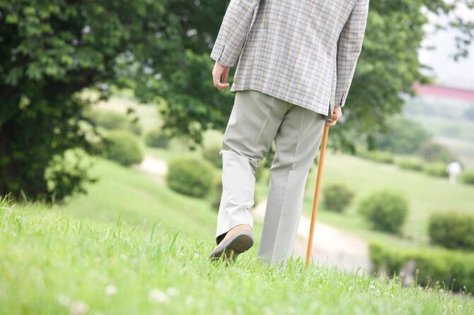 杖を使い公園を散歩する老人
