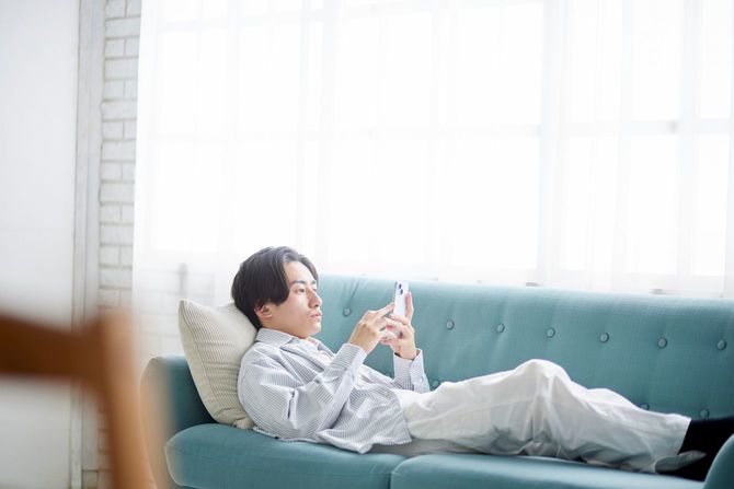 リビングのソファでくつろぎながらスマホを使っている男性