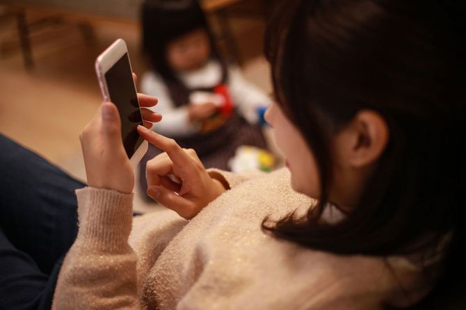 一人で遊ぶ子どもの前でスマホの操作に夢中になる母