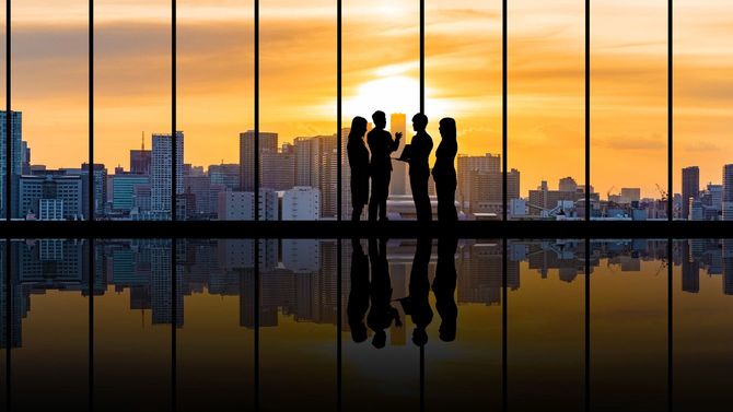 夕陽が差し込む都会のビルの中で話し込むビジネスパーソンのグループ