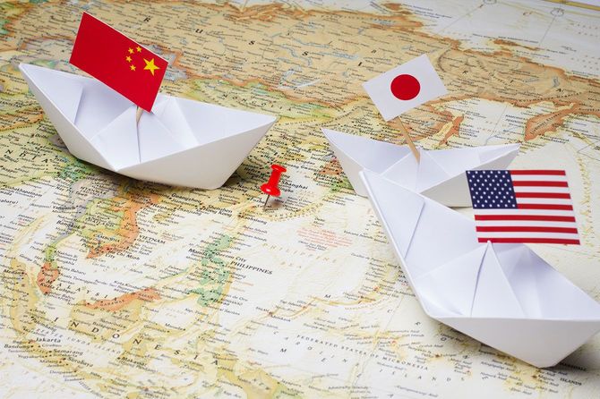 世界地図の上に置かれた、中国、日本、アメリカの国旗が立つ3つの折り紙の船と、台湾付近に刺された押しピン
