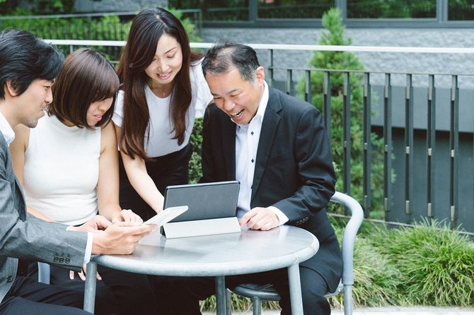 屋外でタブレットを取り囲んで楽しそうな老若男女のビジネスマン