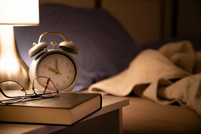 ベッドサイドに書籍と眼鏡と目覚まし時計
