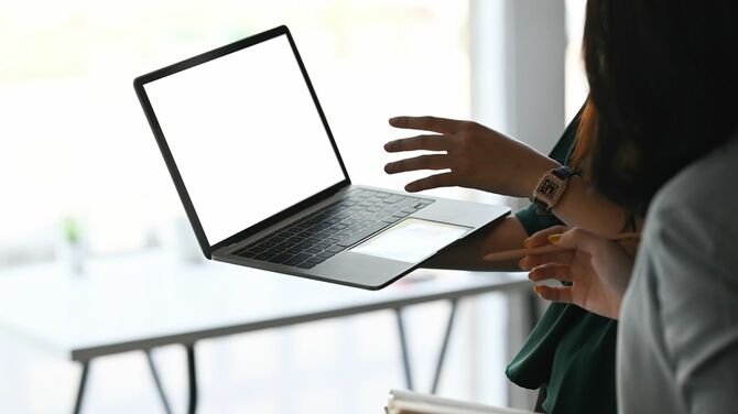 立ったままノートパソコンを片手に説明する女性