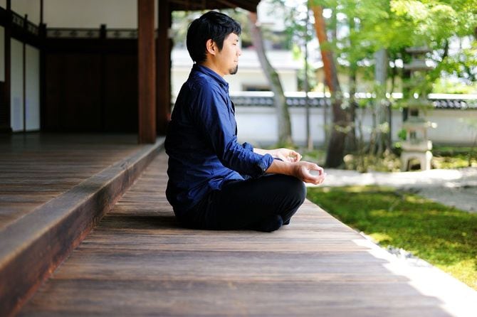 寺院の縁側で座禅を組んで瞑想する男性