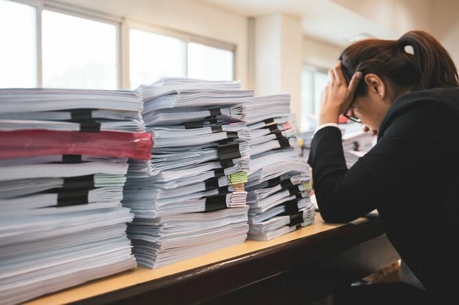 机の上の書類に頭を抱える会社員